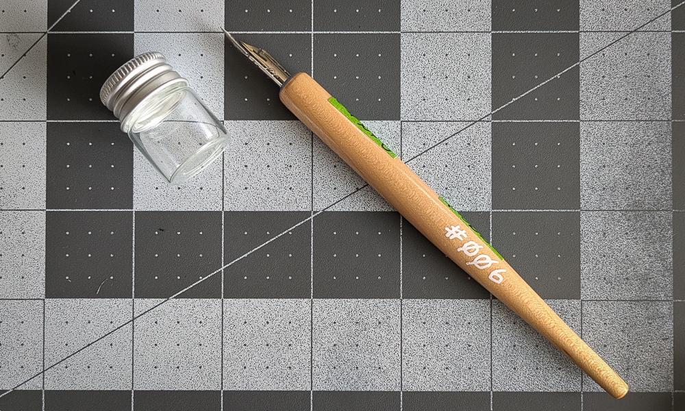 A dip pen next to a very small glass bottle with a screw on lid